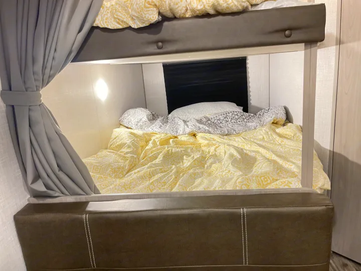 An RV rental's inviting bunk bed, featuring patterned yellow bedding and a grey privacy curtain.. Dutchmen Coleman Lantern LT 2022