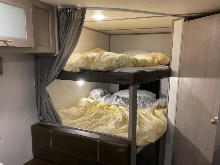 Cozy RV rental interior showing comfortable bunk beds with patterned bedding and privacy curtains.. Dutchmen Coleman Lantern LT 2022