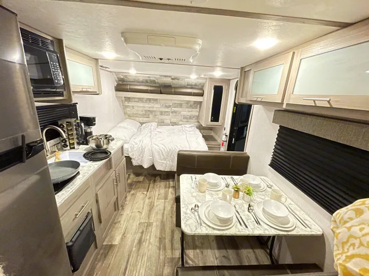 Inside a bright RV rental: full kitchen, cozy bed, and dining booth with a set table. Ideal for your next road trip!. Dutchmen Coleman Lantern LT 2022