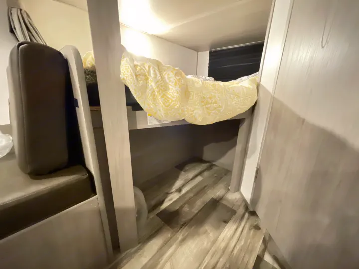 Inside an RV rental: a cozy bunk area featuring patterned yellow bedding, a wood-paneled ceiling, and efficient design.. Dutchmen Coleman Lantern LT 2022