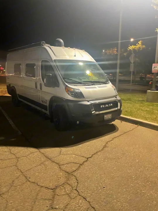 White Ram ProMaster rv rental van parked at night under bright lights in a parking lot, ready for adventure.. Coachmen Nova 2021