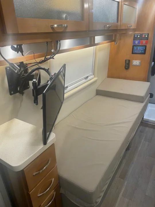A compact RV rental space with a bed, wall-mounted TV, overhead cabinets, and countertop storage.. Coachmen Nova 2021