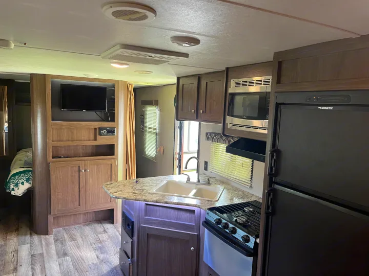 RV rental kitchen and living area, featuring a Dometic fridge, microwave, stove, sink, and TV console.. Keystone RV Hideout 2019
