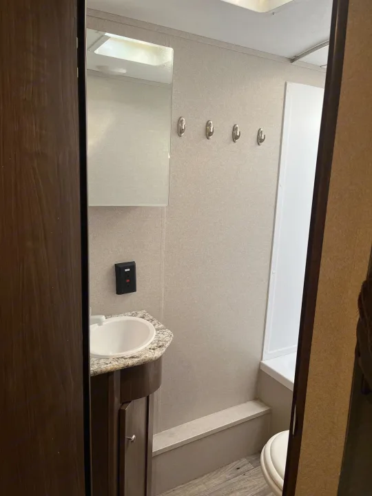Compact RV rental bathroom featuring a sink, large mirror, wall hooks, a bright white shower/tub, and toilet.. Keystone RV Hideout 2019
