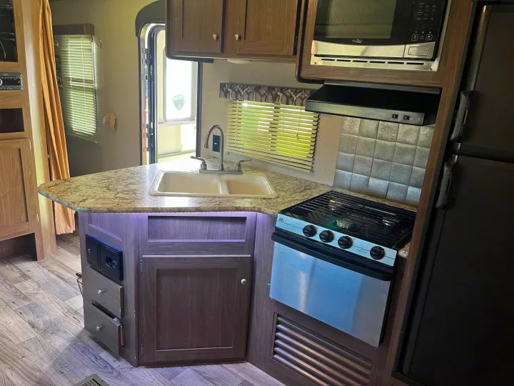 RV rental kitchen: modern with double sink, stove, microwave, and fridge. Features wood-look floors and ample cabinets.. Keystone RV Hideout 2019