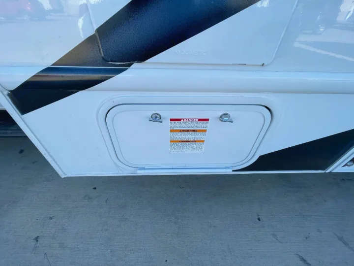 An RV rental's white exterior, featuring a utility access panel with warning labels and Dometic branding.. Thor Freedom Elite 2022