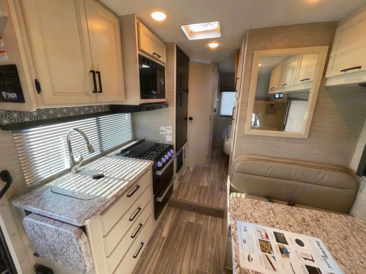 Modern RV rental interior: bright kitchen with sink/stove, dinette, and hallway leading to rear. Compact, functional design.. Thor Freedom Elite 2022