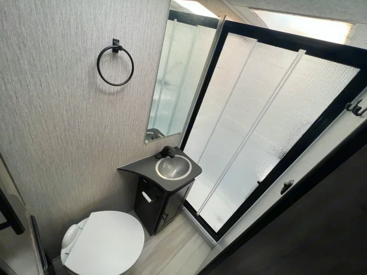 RV rental bathroom featuring a compact toilet, corner sink, and space-saving frosted glass shower. Perfect for on-the-go living.. Coachmen Leprechaun 2021