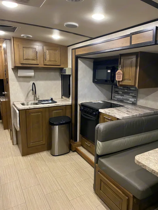 Modern RV rental kitchen & dining area: microwave, stove, sink, wood cabinets, stone-look counters & tile floor.. FR3 FR3 Motorhome 2021