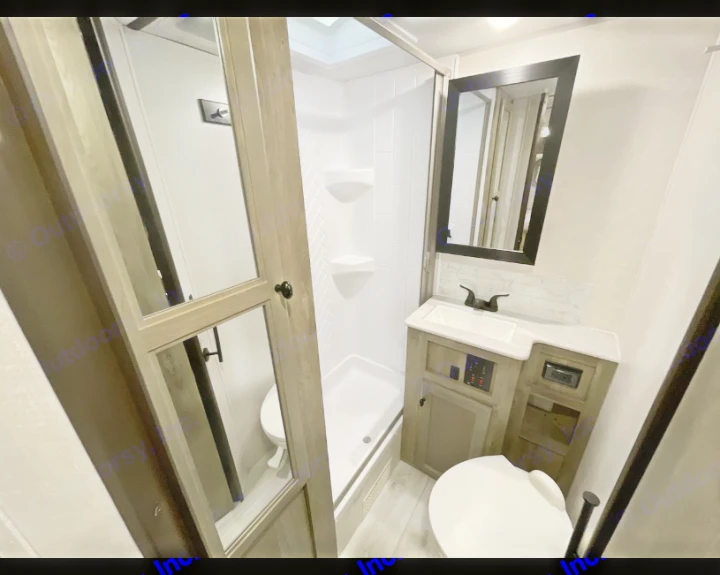 Inside an RV rental: a bright, compact bathroom with a standing shower, vanity with sink & mirror, and toilet. Ideal for travel.. Forest River Surveyor Legend BHLE 2022