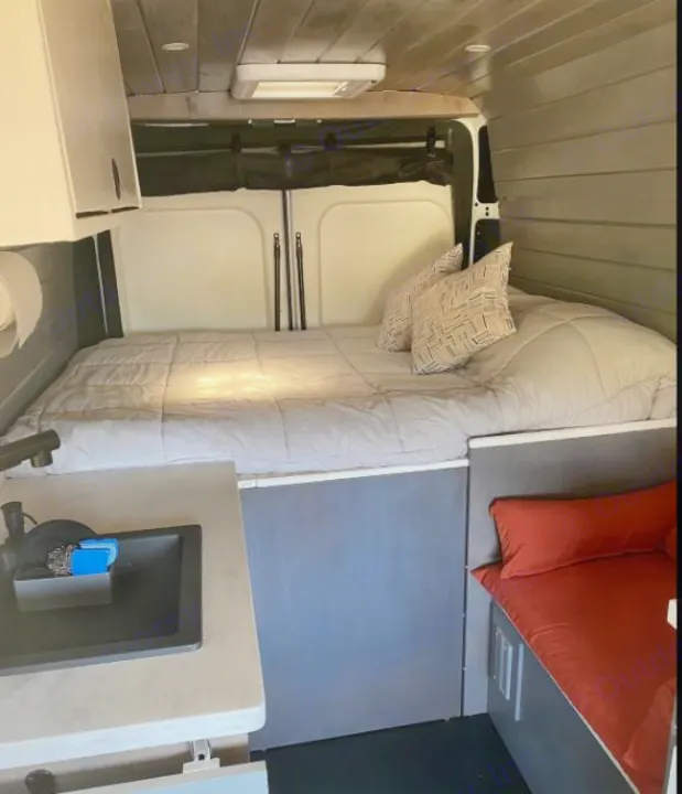Cozy RV rental camper van interior featuring a bed, small kitchen sink, and seating area.. Other Other 2021