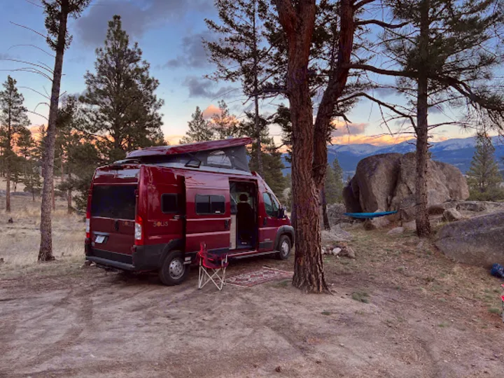 Maroon Winnebago Solis RV rental parked at a rustic mountain campsite with its pop-top extended, offering outdoor comfort.. Winnebago Solis 2022