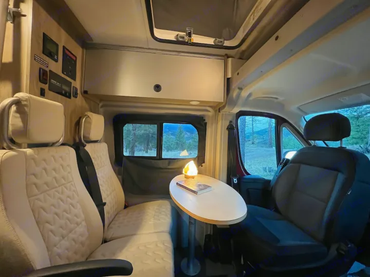 Cozy RV rental interior featuring cream seating, a table with a lamp, and a scenic view of nature outside.. Winnebago Solis 2022