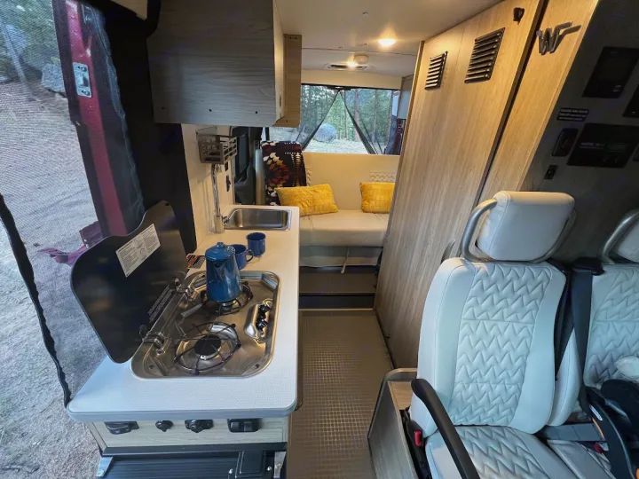 This RV rental's well-equipped interior features a kitchen, comfortable bed, and front seats for travel.. Winnebago Solis 2022