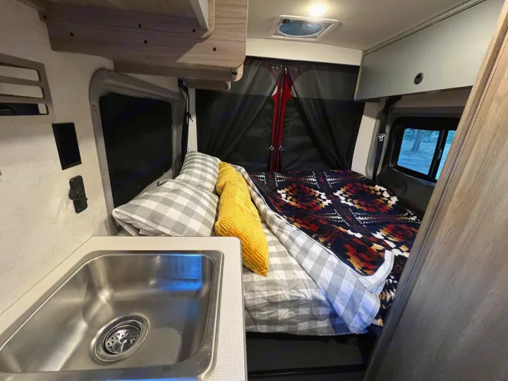 Cozy RV rental interior with a comfy bed, modern sink, and ample storage, ready for your next travel adventure.. Winnebago Solis 2022