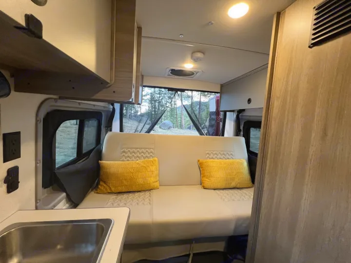Explore this RV rental's cozy interior, featuring a comfortable sofa, overhead cabinets, and natural outdoor views.. Winnebago Solis 2022