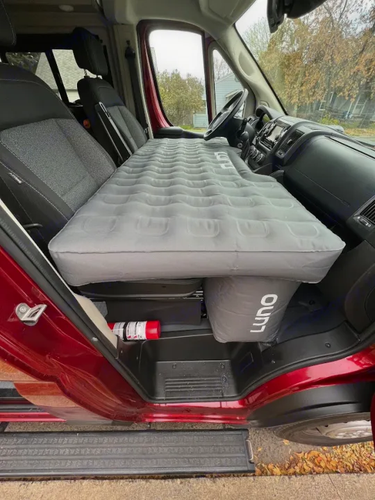 RV rental interior: A Luno air mattress with integrated supports creates a comfortable bed over front seats, fire extinguisher on floor.. Winnebago Solis 2022