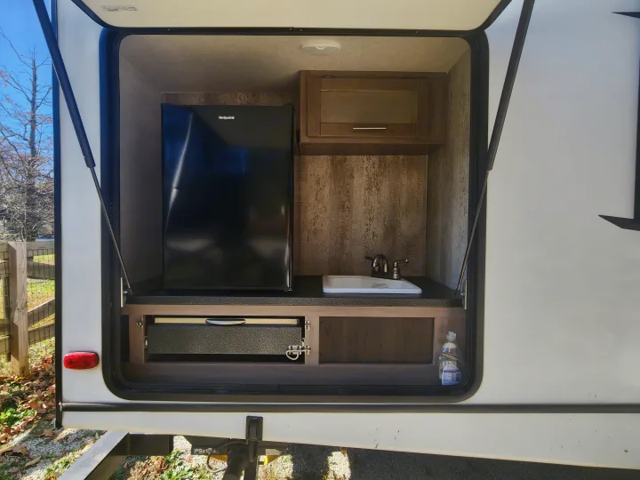RV rental's exterior kitchen, equipped with a Hotpoint mini-fridge, sink, cabinet, and a pull-out cooking unit.. Crossroads Sunset Trail 2021