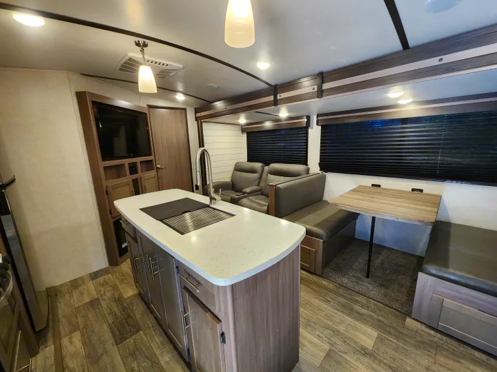 Full interior view of an RV rental with modern kitchen island, comfy recliners, and a dinette.. Crossroads Sunset Trail 2021