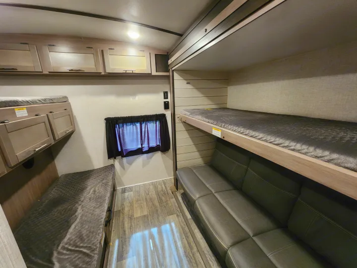 An RV rental's inviting bunk bed area with a comfortable sofa and overhead cabinets, perfect for travel.. Crossroads Sunset Trail 2021