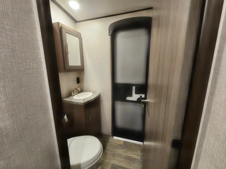 Compact RV rental bathroom featuring a sink, toilet, and mirrored cabinet. The interior is light with wood-look flooring.. Crossroads Sunset Trail 2021