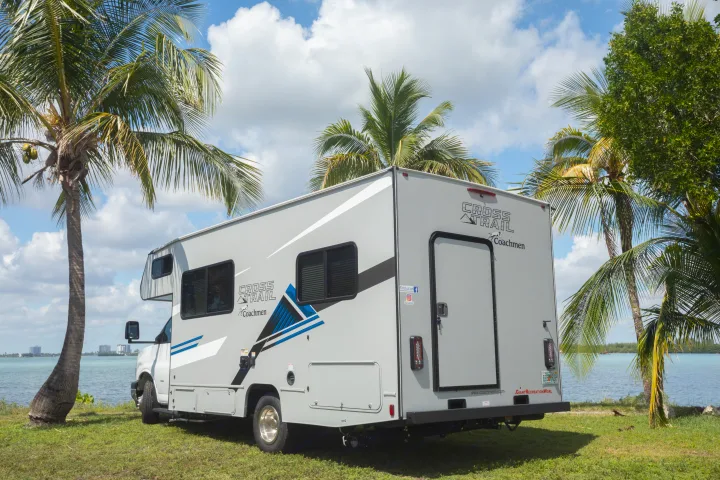 This Coachmen Cross Trail rv rental is parked scenically on grass by the blue ocean, framed by tropical palm trees.. Forest River Coachmen Cross Trail XL 2022