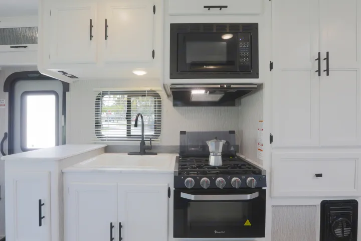 Bright rv rental kitchen featuring white cabinets, sink, microwave, range hood, and stove/oven for travelers.. Forest River Coachmen Cross Trail XL 2022
