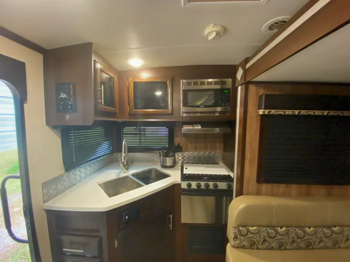 Explore this RV rental kitchen: a compact, modern space with a sink, microwave, stove, and comfortable seating.. Jayco White Hawk 2019