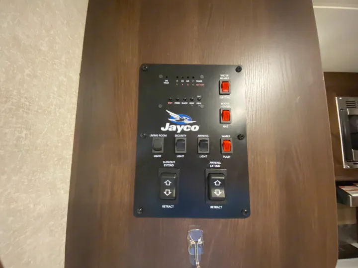 A Jayco RV rental control panel shows water heater, pump, lights, slideout, and awning switches, plus tank/battery levels.. Jayco White Hawk 2019