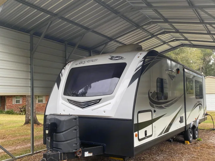 Jayco White Hawk travel trailer parked under a metal carport, ready for an RV rental.. Jayco White Hawk 2019