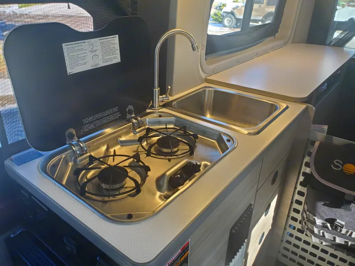Compact kitchen setup in an RV rental, featuring a two-burner stove, a sink with faucet, and countertop space.. Winnebago Solis Pocket 2022