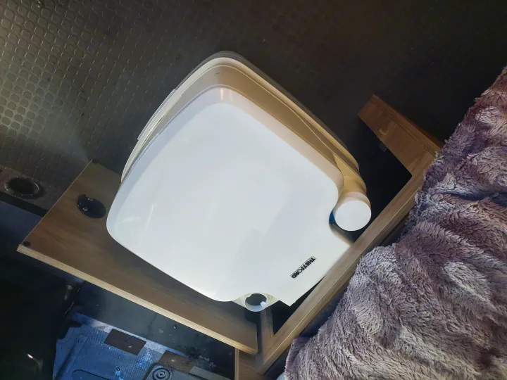 Portable Thetford toilet on a wooden platform in an RV rental, next to a fluffy blanket. Essential for van life.. Winnebago Solis Pocket 2022