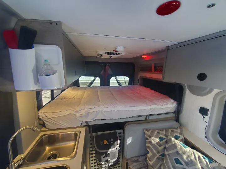 Inside an RV rental featuring a comfy bed, kitchen sink, overhead storage, and geometric pillows.. Winnebago Solis Pocket 2022
