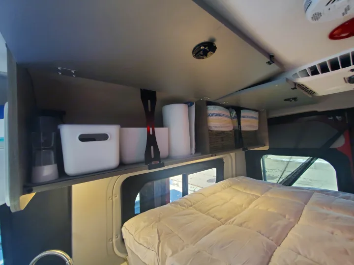 RV rental: Organized overhead shelving with bins & baskets above a cozy bed. Ideal for camper van storage.. Winnebago Solis Pocket 2022