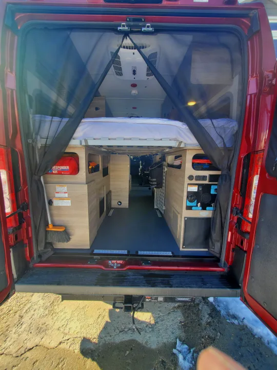 Inside a red camper van for rv rental, showing the bed, storage, utility panel, and mosquito net at the rear.. Winnebago Solis Pocket 2022
