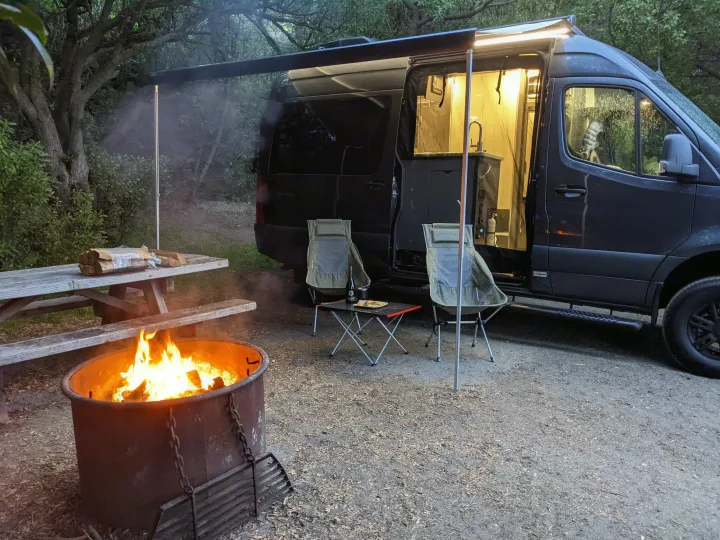 Evening relaxation at an rv rental campsite with a warm campfire, open van, and inviting outdoor seating.. Thor Sanctuary 2022