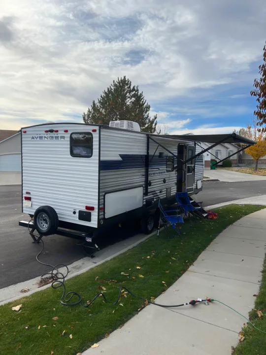 RV rental: travel trailer parked on a street with awning extended, chairs, and power hookups visible.. Prime Time Avenger 2022