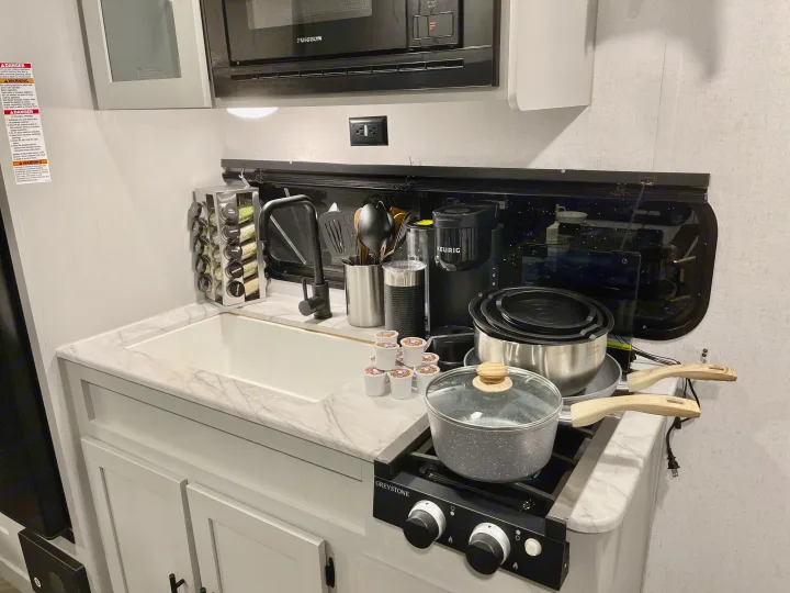 Compact RV rental kitchen with sink, stove, microwave, Keurig, and cooking essentials, ready for convenient travel meals.. Forest River Salem FSX 2021