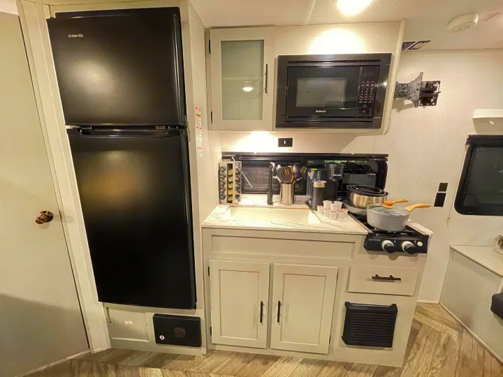 RV rental kitchen: black fridge, microwave, stove, sink, and light cabinetry. Modern RV interior with cooking amenities.. Forest River Salem FSX 2021