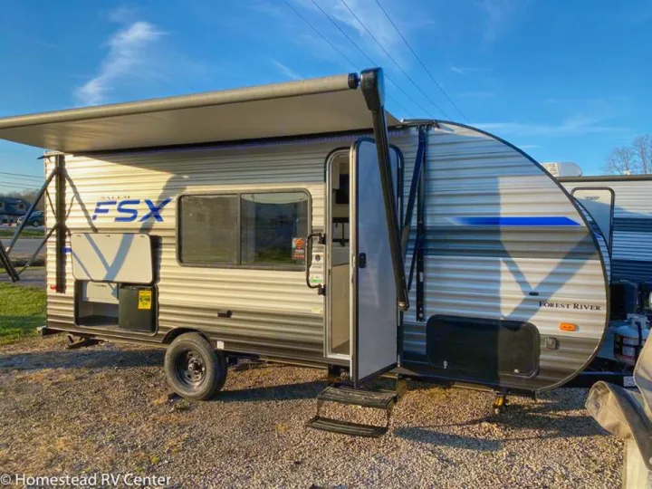 A light-colored Forest River Salem FSX travel trailer with an extended awning and open door. Ideal for RV rental camping trips.. Forest River Salem FSX 2021