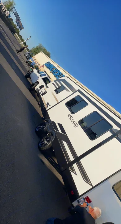 A white Mallard RV travel trailer with a pickup truck at Camping World. Get ready for your next RV rental camping adventure!. Heartland Other 2021
