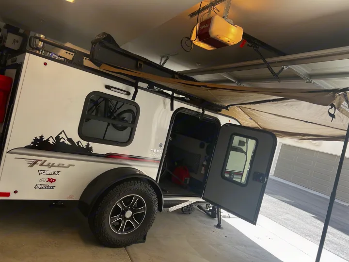 Small Intech Flyer RV rental, a compact travel trailer with an open door and awning, parked in a garage, ready for adventure.. Custom Camper 2021