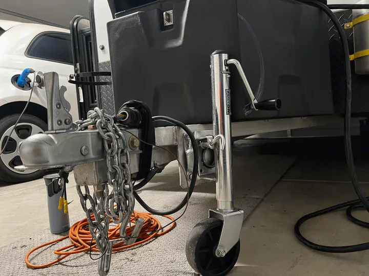 rv rental setup: Trailer hitch, safety chains, jack, and electrical hookup shown. Car charging nearby.. Custom Camper 2021