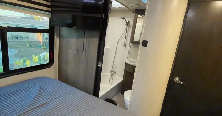 RV rental interior: bedroom area with window and TV, plus a compact bathroom featuring a shower, sink, and toilet.. Heartland Cyclone 2018