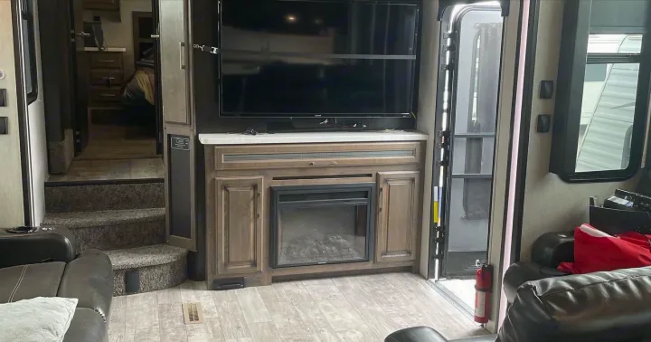 Spacious RV rental interior featuring a living area with TV, fireplace, and steps to an elevated sleeping/private area.. Heartland Cyclone 2018