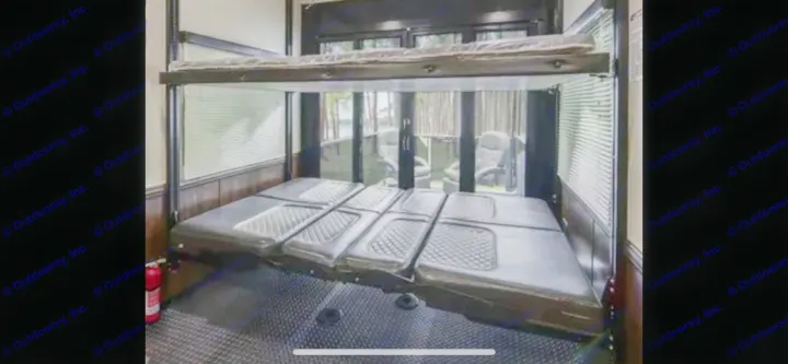 RV rental interior featuring bunk beds & a lower convertible sofa bed. Large windows reveal an outdoor patio with chairs.. Heartland Cyclone 2018