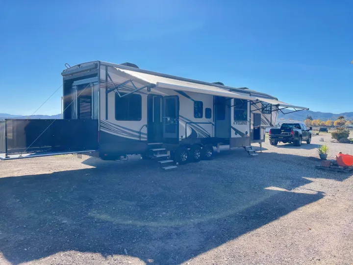 Spacious RV rental, a Cyclone toy hauler, set up on a gravel lot with extended awnings, perfect for outdoor trips.. Heartland Cyclone 2018
