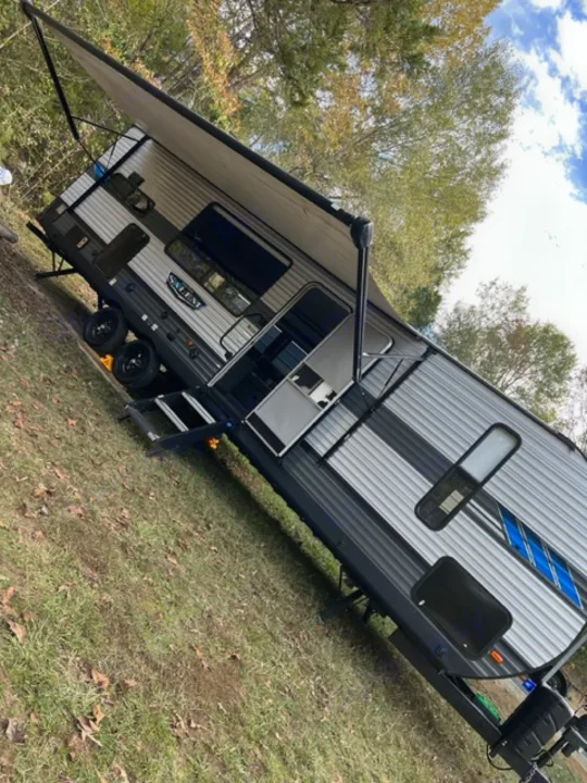 A modern Salem travel trailer RV rental with an extended awning, parked in a grassy area amidst trees for camping.. Forest River Salem 2021