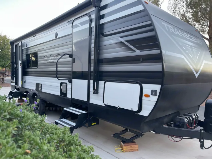 A modern Transcend travel trailer for RV rental adventures, parked at a campsite with steps down & stabilizers deployed.. Grand Design Transcend Xplor 2022