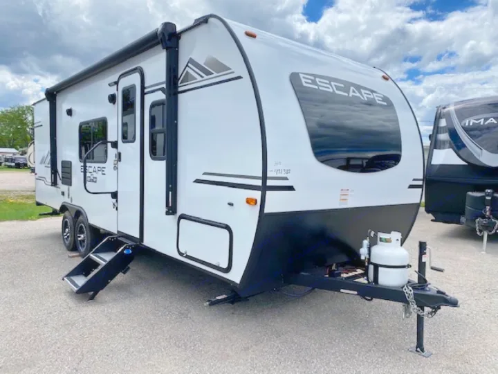 White Escape travel trailer RV rental, parked outdoors. Features front window, side door, and propane tanks.. Escape e231bh 2022